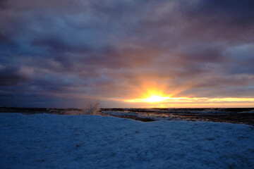 Wall Mural - ice splashes at the sea on a cold winter sunset with snow and clouds in the sky