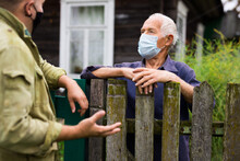 Elderly Man In Mask Discussing With Neighbour Beside House
