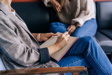 Close-up Of A Psychologist's Hands Writing Down Notes About A Patient In A Notebook. The Psychologist Makes A Social Survey Of The Reference Group. A Professional Is Talking To A Client.