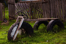 Rustic Bench In The Form Of A Three-wheeled Car Against The Background Of A Rickety Fence