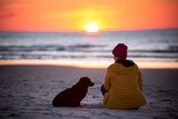 Fototapeta Fototapety z morzem do Twojej sypialni - Dziewczyna i pies siedzą na plaży 