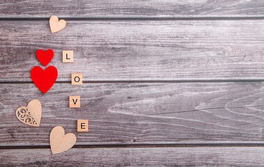 Wooden natural and red decorative hearts and letters love on wooden background top view. Copy space