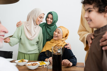 Canvas Print - Positive multiethnic women talking near food and family at home.