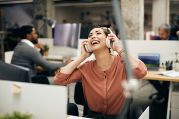 Wall Mural - Carefree businesswoman enjoys in music over headphones in the office.