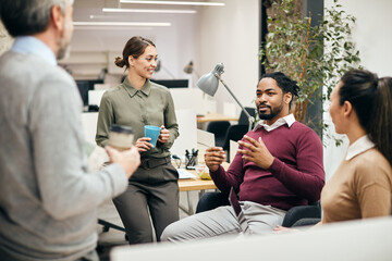 Wall Mural - Black businessman enjoys in conversation with his Caucasian colleagues during coffee break at corporate office.