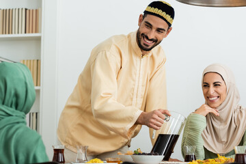 Poster - happy muslim man in skullcap pouring tea near happy woman in hijab.