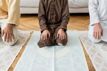 Wall Mural - Cropped view of preteen muslim boy sitting on rug near family.