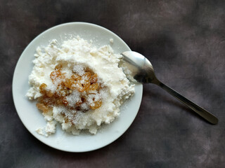 cottage cheese with raisins on a plate with a spoon on a dark vintage background top view