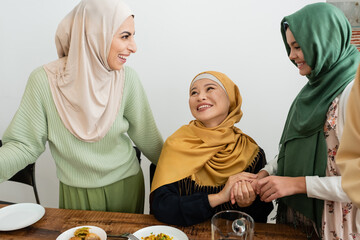 Poster - Smiling arabian woman looking at daughter and asian mom near food at home.