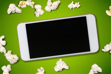 Sticker - Smartphone with blank screen and popcorn on the background. Streaming media and video-on-demand online