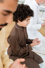 Poster - Curly arabian boy praying near father and grandparent at home.