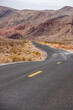 Overton, Nevada, USA - February 24, 2010: Valley of Fire. Black asphalt uneven road with yellow lines pulls a line in dry desert landscape with brown mountain range in back under gray sky.