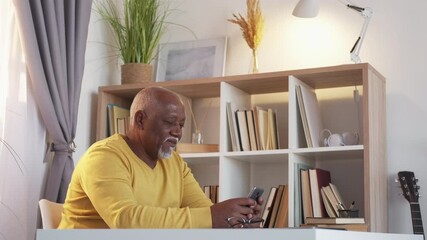 Social network. Happy senior man. Virtual connection. Positive african aged guy scrolling smartphone sitting desk in light room interior.