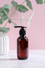 Wall Mural - Dark amber glass cosmetic dispenser bottle and eucalyptus branch on pink background. Organic shampoo packaging design, branding.