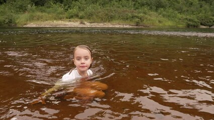 cute little girl sitting in a river jumps up and dives in, slow motion.