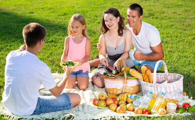 Wall Mural - Happy parents with two kids having picnic together on green meadow in park. High quality photo