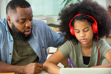 Wall Mural - African family spending time together at home. Father helping little daughter online study on laptop computer in living room. Cute child girl kid studying homeschooling with using online E-learning