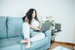 Young freelancer latina woman working on computer while sitting on the comfortable sofa at home on modern trendy clothes. Concept of remote work from home, young people online works