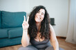 Full length shot of young curvy woman in sportswear sitting floor resting while doing fitness yoga at home. victory sign. Losing weight at home. Online class with the laptop concept. Long curly hair