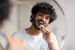 © Prostock-studio - Oral care concept. Young indian man cleaning teeth with toothbrush, smiling to his reflection in mirror