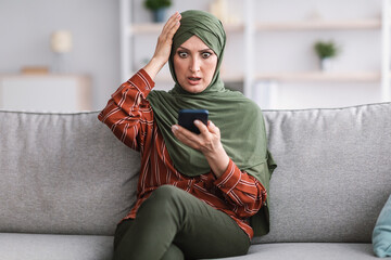 Wall Mural - Shocked Muslim Woman Holding Smartphone Touching Head At Home