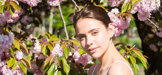 Girl in in blossoms cherry sakura. Outdoor portrait of beautiful sensual fashion girls posing near blooming tree with pink flowers. Spring design for banner or website header.