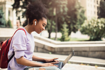 Wall Mural - Happy African American Student Girl Browsing Internet On Laptop Outdoors