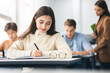 © Prostock-studio - Smiling woman sitting at desk in classroom writing in notebook