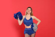 Beautiful cheerleader in costume holding pom poms on red background