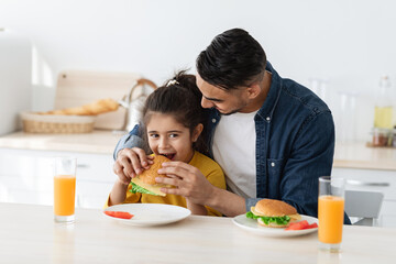 Wall Mural - Daddy's Care. Young Arab Father Feeding Little Daughter With Sandwich In Kitchen