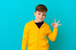 © luismolinero - Little redhead boy isolated on blue background showing ok sign with fingers