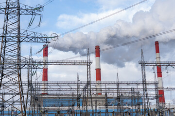 Smoke from three white-red chimneys against a blue sky and a nearby power plant.