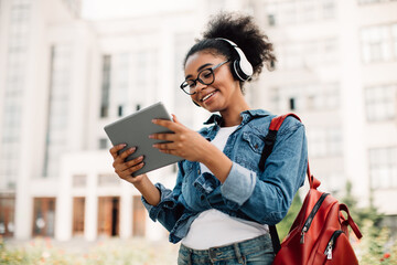 Wall Mural - Happy Black Female Student Using Tablet Computer Wearing Headphones Outside