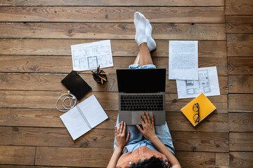 Top view of young lady with laptop, study or work materials and tablet pc sitting on wooden floor indoors, mockup