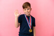 Little redhead boy with medals isolated on pink background saluting with hand with happy expression