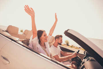 Photo of funny carefree husband wife wear white outfits riding automobile rising arms outside urban city route