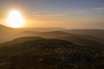 Wall Mural - Welsh mountain summit at sunset with a man standing next to his tent with glorious views