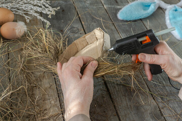 Handmade master class Easter nest made of natural dry grass and used cardboard. The hands of an elderly woman show step by step how to make an Easter nest on wood background