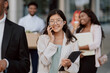 © ABCreative - Young beautiful office worker with glasses finishes work goes outside in front of company building with co-workers, holds tablet in hand, answers phone, talks with friend