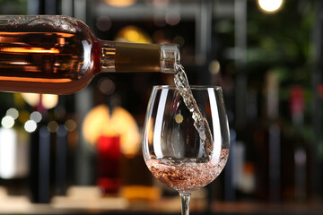 Pouring rose wine from bottle into glass on blurred background, closeup