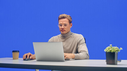 Poster - Modern Office Green Screen Background: Young Businessman Sitting at His Desk Working on a Laptop Computer. Man working with Big Data e-Commerce Analysis.