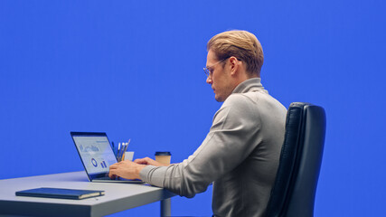 Wall Mural - Modern Office Green Screen Background: Businessman Sitting at His Desk Working on a Laptop Computer. Man working with Big Data e-Commerce Analysis. Over the Shoulder Shot.