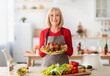 © Prostock-studio - Cheerful elderly woman in apron holding dish with roasted turkey for Christmas or Thanksgiving holiday in kitchen