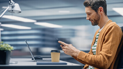 Poster - Modern Office: Businessman Sitting at His Desk Using Smartphone, Laptop Computer. Digital Entrepreneur working with Big Digital Data e-Commerce. Motion Blur Background Showing Active Work Day.