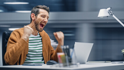 Poster - Modern Office: Businessman Sitting at His Desk Works on Laptop Computer, Celebrate Success. Digital Entrepreneur working with e-Commerce App Smiles, Happy Victory. Motion Blur Background