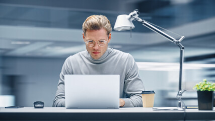 Poster - Modern Office: Productive Businessman Sitting at His Desk Working on a Laptop Computer. Man working with Big Data e-Commerce Analysis. Energetic Shot with Motion Blur Background