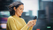© Gorodenkoff - Street Shot: Portrait of Beautiful Latin Woman Using Smartphone. Smiling Hispanic Female Entrepreneur Using Mobile Phone for Online Shopping, e-Commerce Happily. Blurred Motion Background.