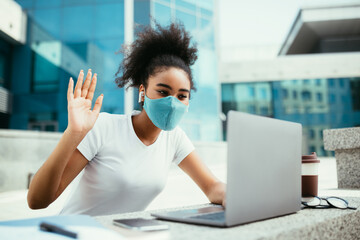 Wall Mural - African female student video calling wearing mask in urban area