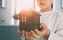 Kid Holding Wooden Toy House In Hands. Adoption Concept. Desire To Have Your Own Home And Family.
