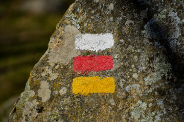 White, red and yellow signs for hikers on a stone of a path.